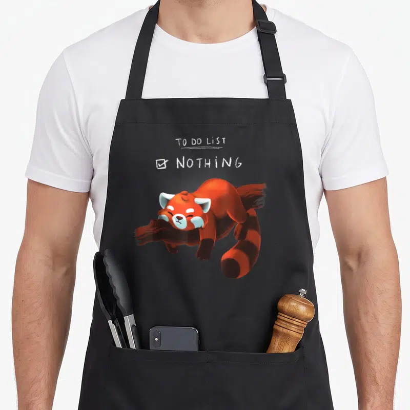 Panda animal apron - To Do List Nothing text above a lying orange-red cartoon red panda with white ears — shown on a black cotton canvas apron against a white background