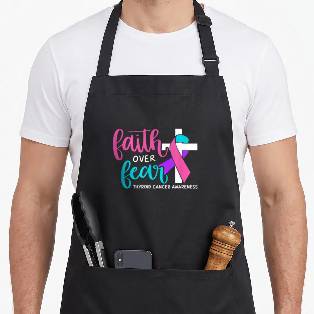Religious thyroid apron - Faith over fear text with white cross and pink cyan ribbon — shown on a black cotton canvas apron against a white background