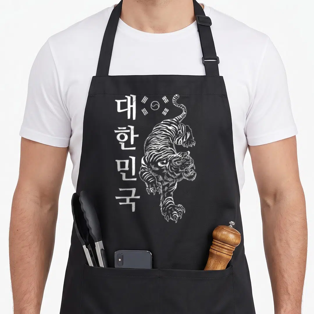 Korea girls korean apron - White line-art tiger next to vertical Korean text and Taegeuk symbol — shown on a black cotton canvas apron against a white background