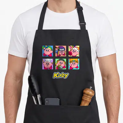 Selected pop apron - Six square panels of pink Kirby in different costumes with yellow Kirby text below — shown on a black cotton canvas apron against a white background
