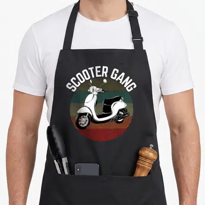 Gang scooter apron - Retro scooter illustration with arched SCOOTER GANG text over yellow teal and red halftone circle — shown on a black cotton canvas apron against a white background