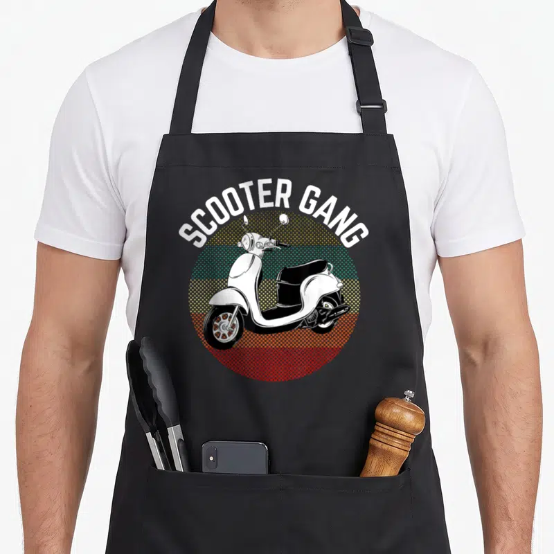 Gang scooter apron - Retro scooter illustration with arched SCOOTER GANG text over yellow teal and red halftone circle — shown on a black cotton canvas apron against a white background
