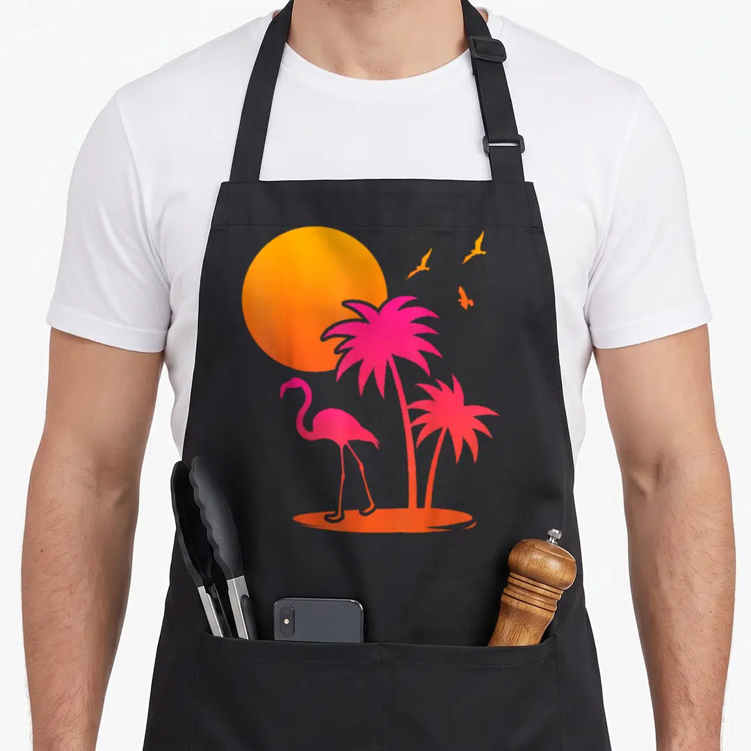 Summer palm pink flamingo apron - Pink flamingo and two palm tree silhouettes under an orange sun with three birds — shown on a black cotton canvas apron against a white background