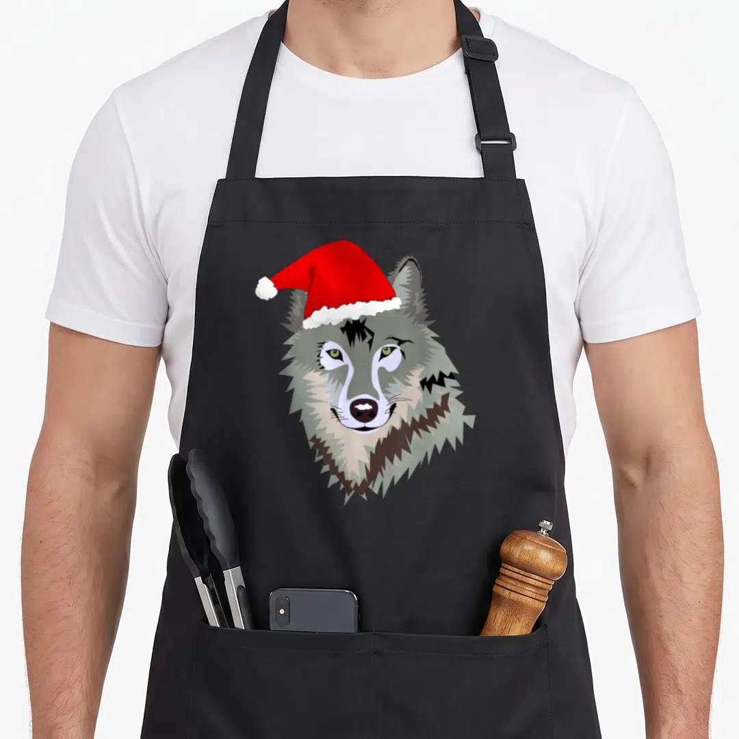 Wolf santa aprons - Cartoon grey wolf head wearing red Santa hat tilted left, no text — shown on a black cotton canvas apron against a white background