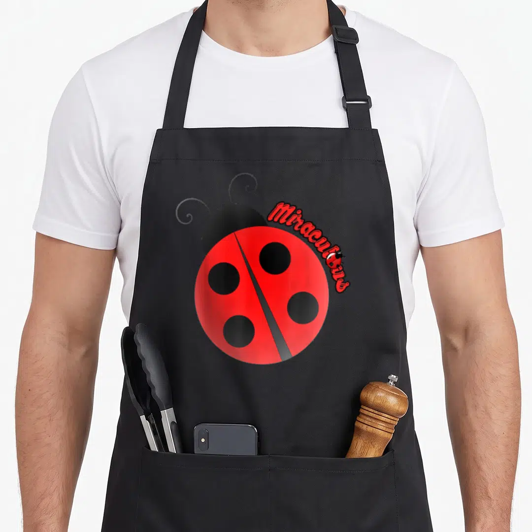 Miracle ladybug apron - Red cartoon ladybug with four black spots and curved Miraculous text on upper right shell — shown on a black cotton canvas apron against a white background