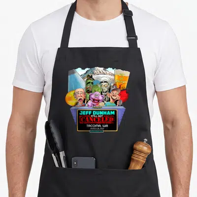 Jeff north boy apron - Jeff Dunham Still Not Canceled Tacoma 2023 cartoon characters grey podium — shown on a black cotton canvas apron against a white background
