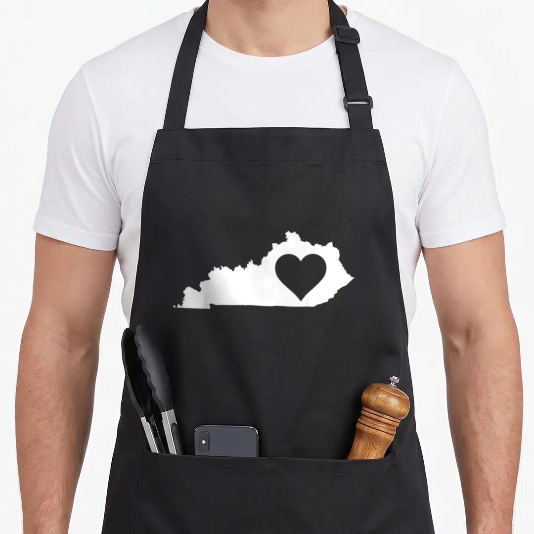 Funny kentucky boy apron - White Kentucky state map silhouette with heart cutout on grey background — shown on a black cotton canvas apron against a white background