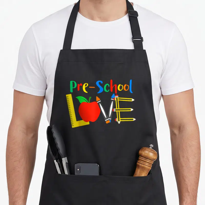 Pre classroom aprons - Pre-School text above LOVE made of ruler, red apple, two pencils, three pencils in red yellow — shown on a black cotton canvas apron against a white background