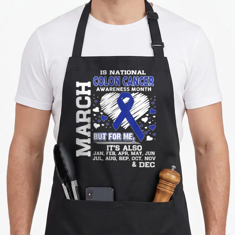 March colon cancer awareness apron - Blue ribbon over white heart with text listing all months for colon cancer support — shown on a black cotton canvas apron against a white background