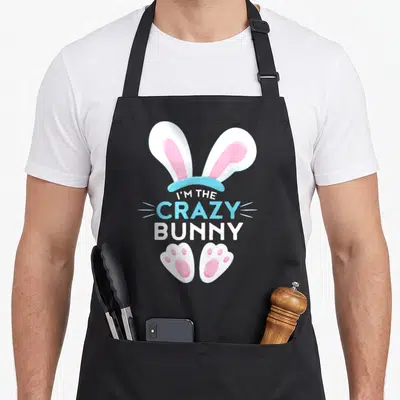 Cool family easter bunny aprons - Cartoon bunny ears and paws in white pink and blue surrounding stacked text I'M — shown on a black cotton canvas apron against a white background