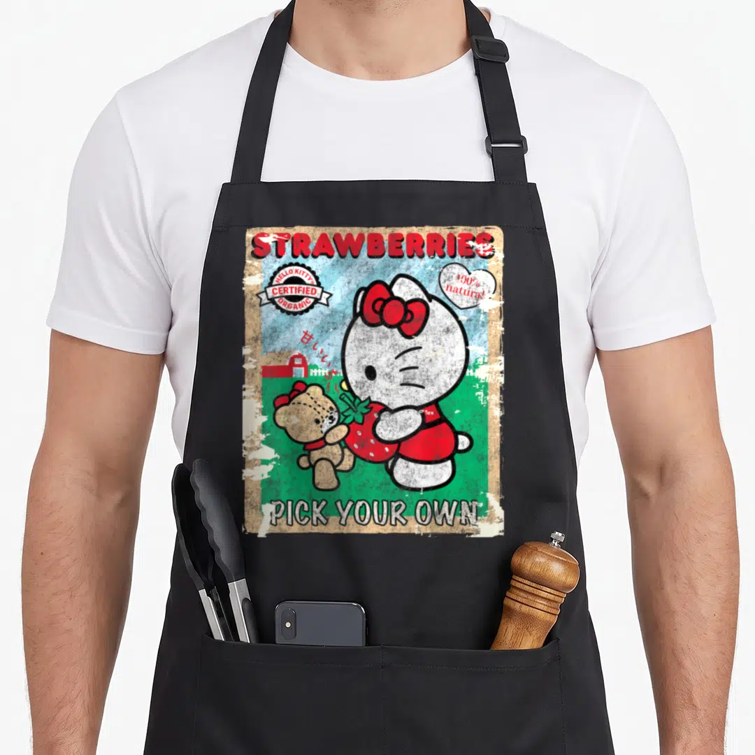 Picking strawberry apron - Hello Kitty and teddy bear holding red strawberry with barn, clouds, and distressed vintage — shown on a black cotton canvas apron against a white background