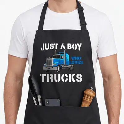 Birthday semi truck apron - Blue cartoon semi truck with stenciled text JUST A BOY WHO LOVES TRUCKS in white and grey — shown on a black cotton canvas apron against a white background