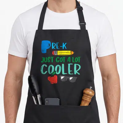 Cooler day pre apron - PRE-K text with pencil apple and sunglasses in cartoon style — shown on a black cotton canvas apron against a white background