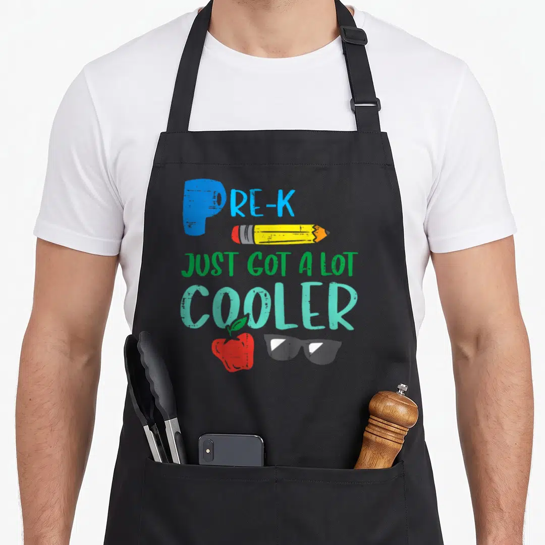 Cooler day pre apron - PRE-K text with pencil apple and sunglasses in cartoon style — shown on a black cotton canvas apron against a white background