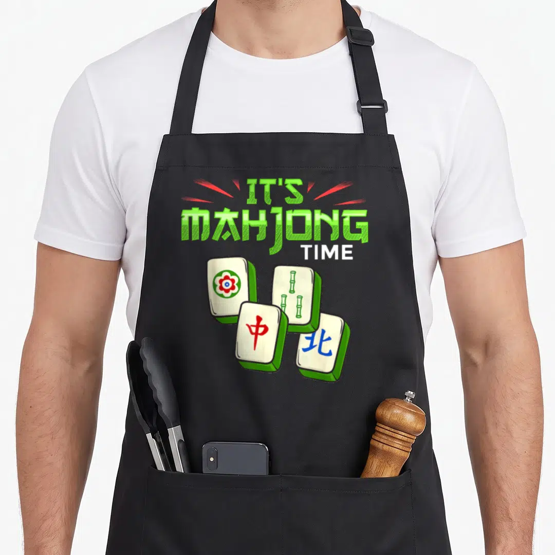 Game mah mahjong apron - Green IT'S MAHJONG TIME text above four white tiles with red flower, bamboo, red character — shown on a black cotton canvas apron against a white background