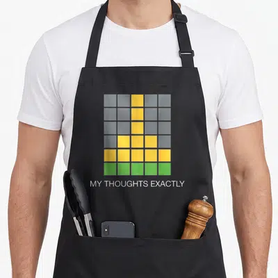 Wordle game aprons - Grid of yellow and green sticky notes above white text MY THOUGHTS EXACTLY on grey background — shown on a black cotton canvas apron against a white background