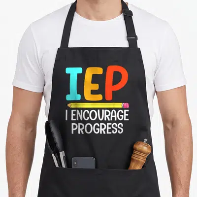 Iep sped teacher apron - Colorful IEP letters above yellow pencil and white I Encourage Progress text — shown on a black cotton canvas apron against a white background