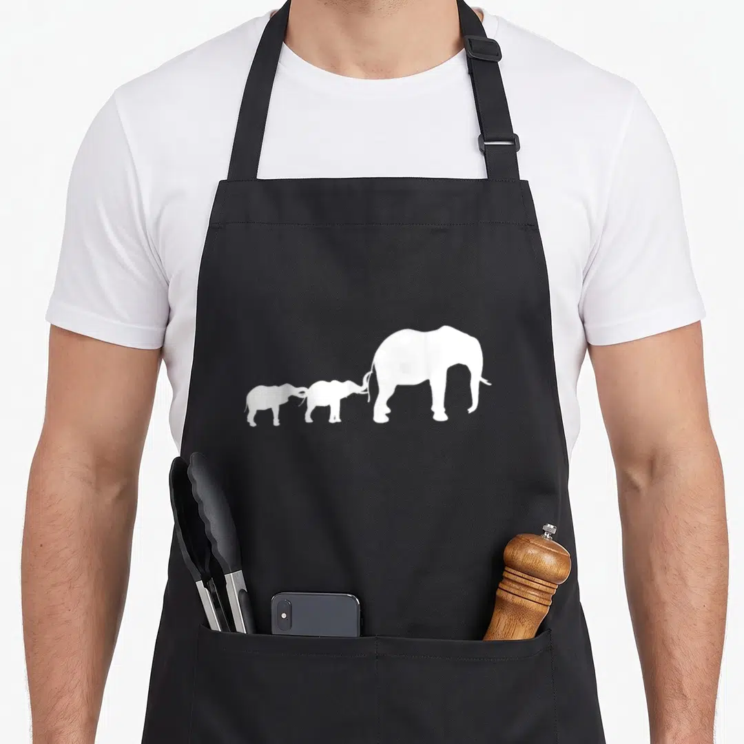 Africa mother's apron - Three white elephant silhouettes in a row facing right, smallest left touching largest tail — shown on a black cotton canvas apron against a white background
