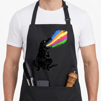 Tyrannosaurus shooting apron - Sitting black cartoon dinosaur breathing a rainbow stream of blue orange yellow pink — shown on a black cotton canvas apron against a white background