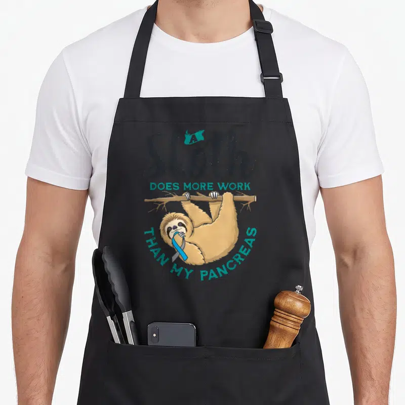 Diabete sloth apron - Cartoon sloth hanging from branch holding blue ribbon with text about pancreas work — shown on a black cotton canvas apron against a white background