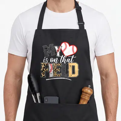 Softball leopard apron - Leopard print text reading MY is on that FIELD with heart baseball graphic — shown on a black cotton canvas apron against a white background