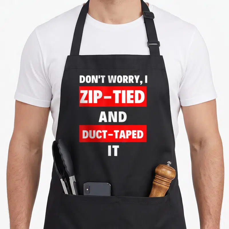 Worry jdm lover apron - White text in red blocks reading DON'T WORRY I ZIP TIED AND DUCT TAPED IT — shown on a black cotton canvas apron against a white background