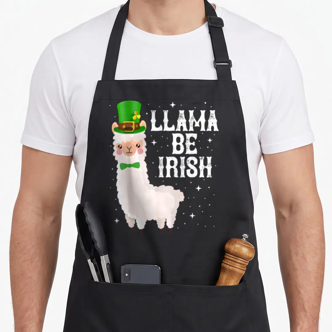 Llama st patrick day aprons - Cartoon white llama in green hat and bow tie beside stacked text LLAMA BE IRISH on grey — shown on a black cotton canvas apron against a white background