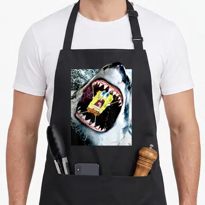 Squarepant shark apron - Cartoon character inside realistic shark mouth with grey and yellow accents — shown on a black cotton canvas apron against a white background