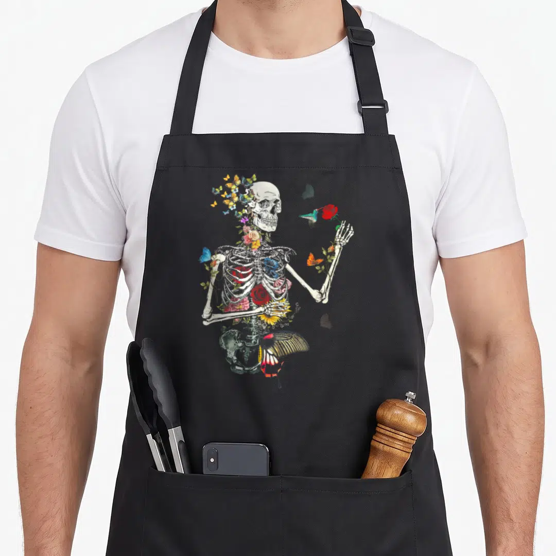 Nature plant apron - Realistic skeleton torso decorated with red, blue, yellow, and off-white flowers and a hummingbird — shown on a black cotton canvas apron against a white background