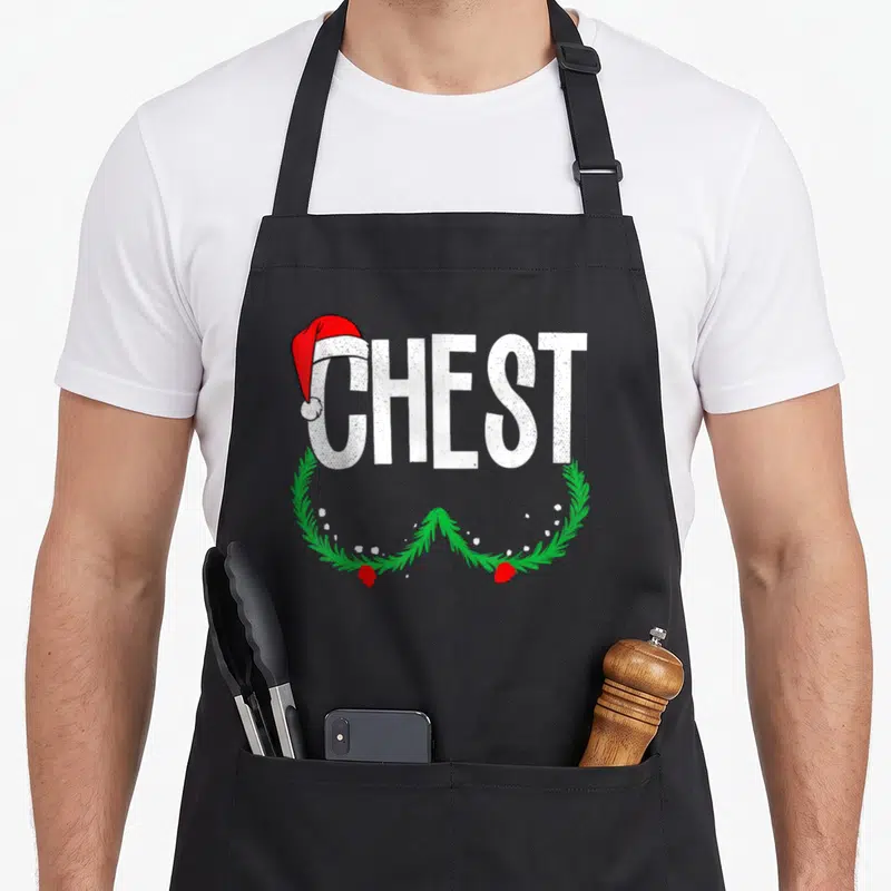 Vintage chestnut couples christmas aprons - White CHEST text with red Santa hat and green pine berry wreath — shown on a black cotton canvas apron against a white background