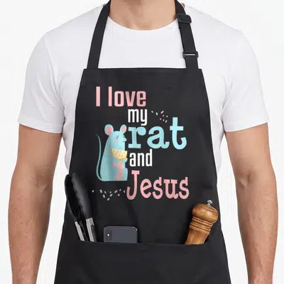 Rat christian apron - Cartoon blue rat holding yellow slice next to pink and white stacked text with confetti — shown on a black cotton canvas apron against a white background