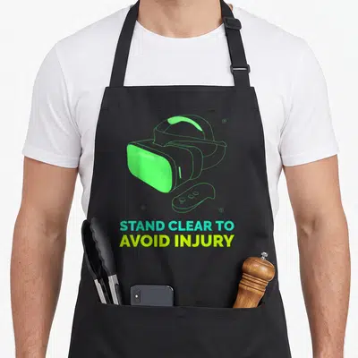 Virtual clear apron - VR headset and controller outline with STAND CLEAR TO AVOID INJURY text in lime and cyan — shown on a black cotton canvas apron against a white background