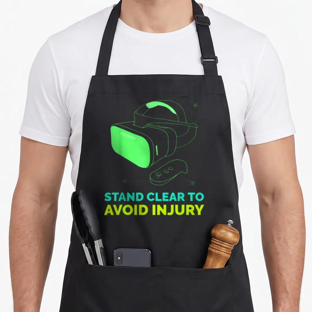 Virtual clear apron - VR headset and controller outline with STAND CLEAR TO AVOID INJURY text in lime and cyan — shown on a black cotton canvas apron against a white background