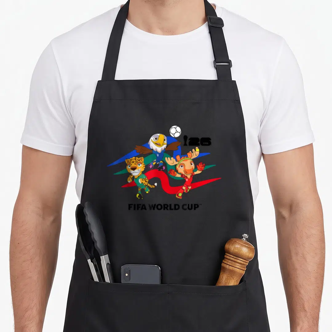 Mascot country apron - Three cartoon mascots with soccer ball and FIFA WORLD CUP text over blue, green, red, and yellow — shown on a black cotton canvas apron against a white background