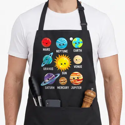 Solar space planets apron - Cartoon sun and planets labeled MARS NEPTUNE EARTH URANUS SUN VENUS SATURN MERCURY JUPITER — shown on a black cotton canvas apron against a white background