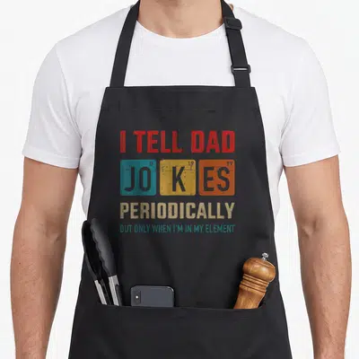 Periodically father day apron - Red teal yellow grey stacked text with three element-style squares spelling JO K ES — shown on a black cotton canvas apron against a white background
