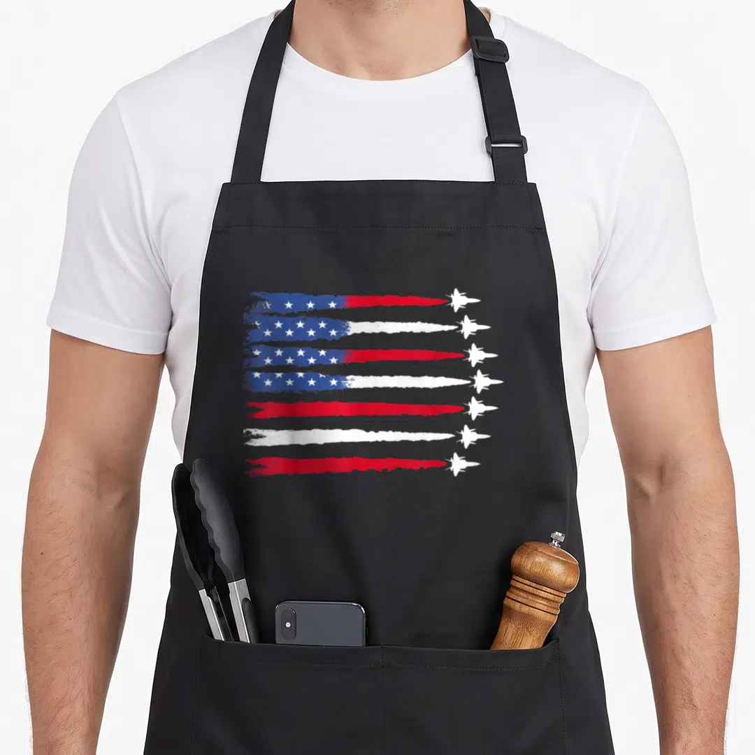 Fighter 4th of july apron - Seven white jets leaving distressed smoke trails forming a US flag pattern in red white — shown on a black cotton canvas apron against a white background