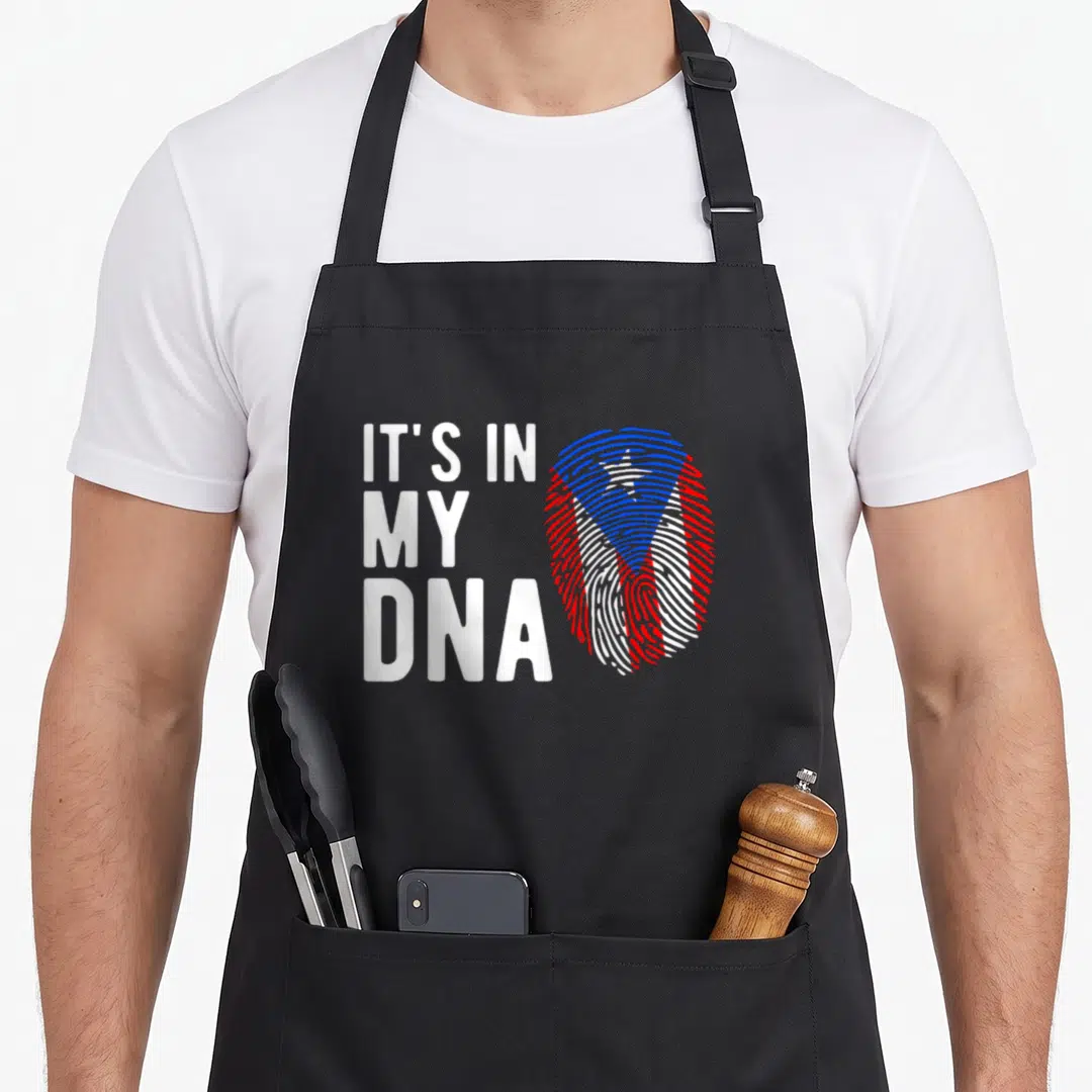 Dna puerto boy apron - Stacked white text IT'S IN MY DNA next to a red white and blue fingerprint pattern — shown on a black cotton canvas apron against a white background