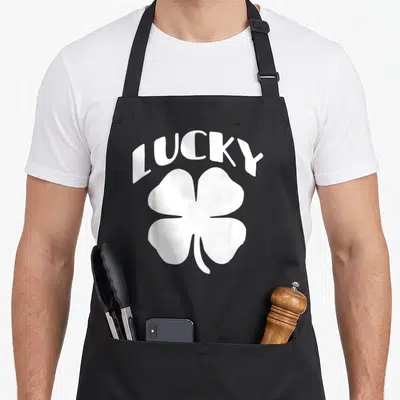 Lucky special aprons - White arched LUCKY text above a four-leaf clover graphic on grey background — shown on a black cotton canvas apron against a white background