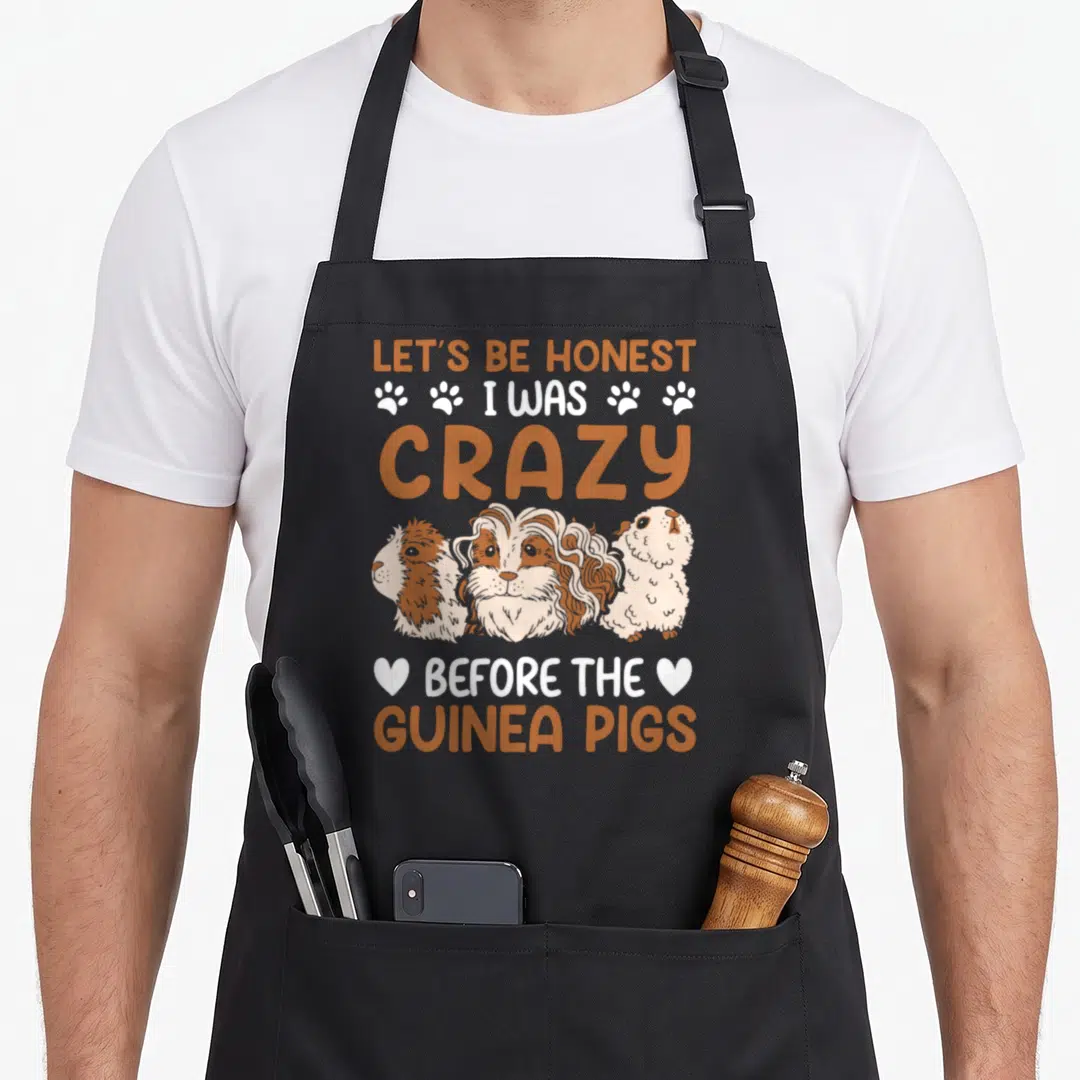 Honest before crazy guinea man apron - Three cartoon guinea pigs with orange text and white paw prints — shown on a black cotton canvas apron against a white background