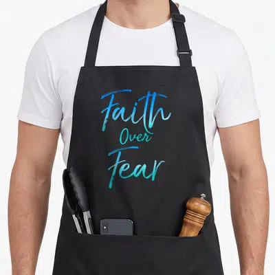 Inspired christian apron - Stacked blue and teal script reading Faith Over Fear on black fabric — shown on a black cotton canvas apron against a white background