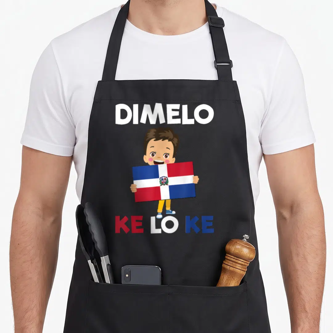 Republic dominican girl apron - Cartoon boy holding Dominican flag with DIMELO KE LO KE text in white red blue brown — shown on a black cotton canvas apron against a white background