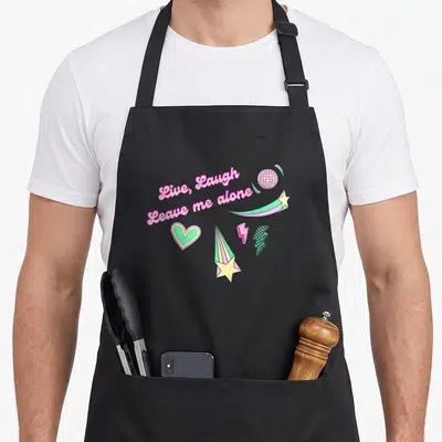 Disco live laugh leave apron - Pink text reading Live Laugh Leave me alone with disco ball and stars — shown on a black cotton canvas apron against a white background