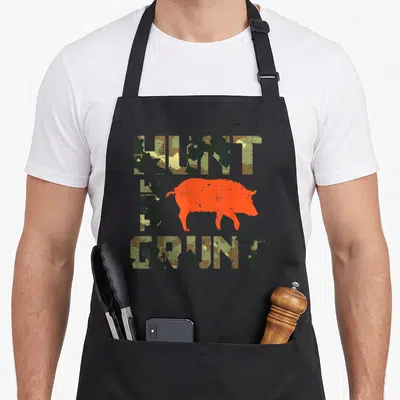 Hunt camo apron - Orange wild boar silhouette surrounded by camo text reading HUNT THE GRUNT — shown on a black cotton canvas apron against a white background