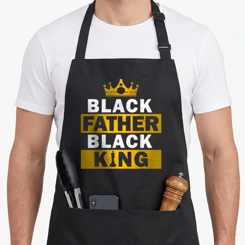King father day apron - Crown above stacked BLACK FATHER BLACK KING text with chess piece replacing I in KING — shown on a black cotton canvas apron against a white background