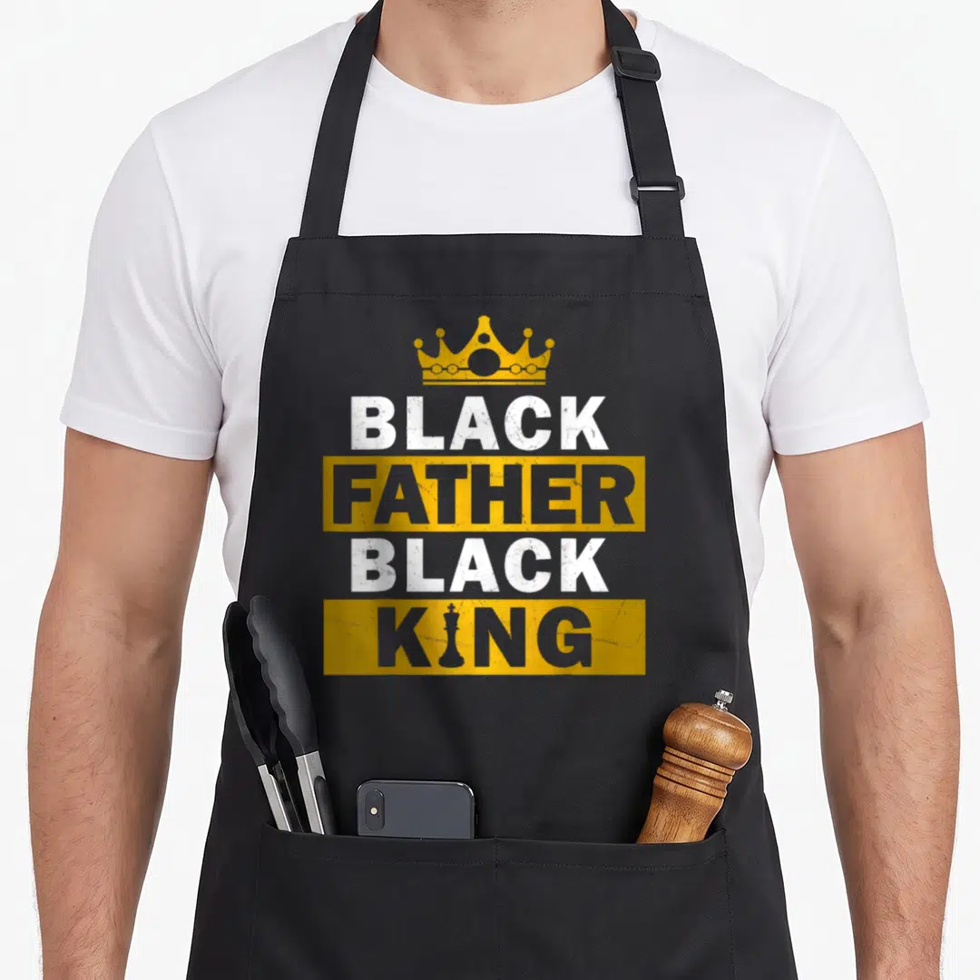 King father day apron - Crown above stacked BLACK FATHER BLACK KING text with chess piece replacing I in KING — shown on a black cotton canvas apron against a white background