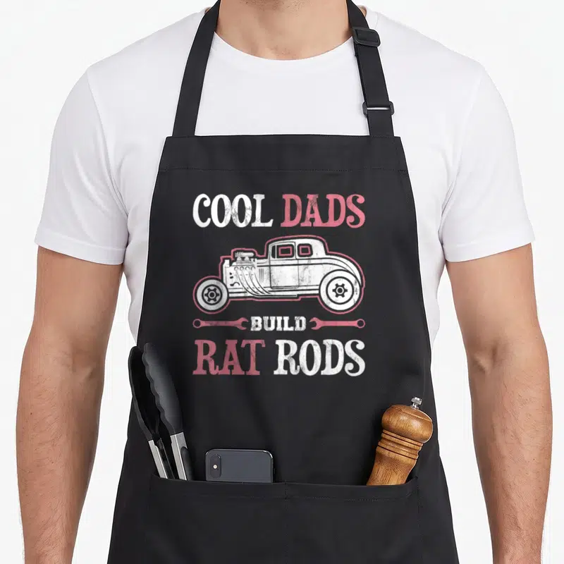 Build rat dad apron - Cool Dads Build Rat Rods text with rat rod side view and two wrenches in white and red distressed — shown on a black cotton canvas apron against a white background