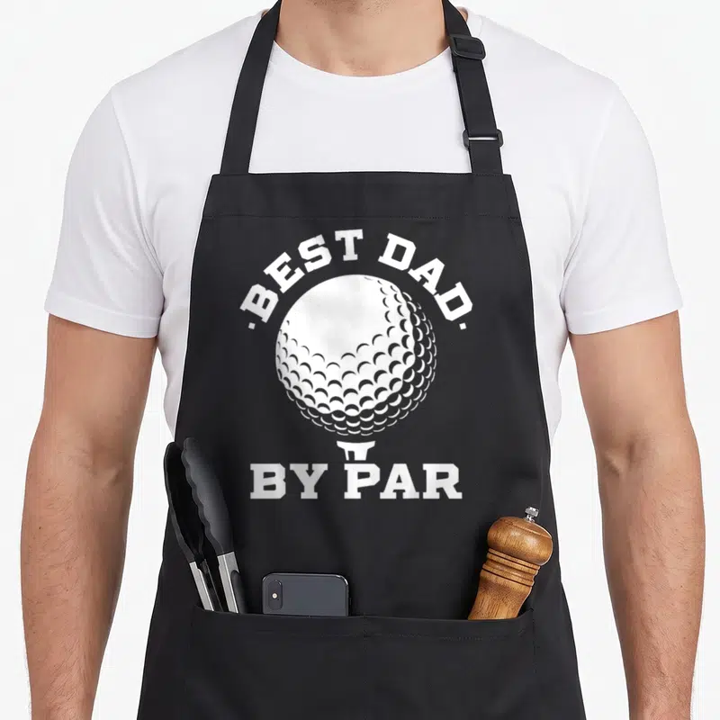 Player father day apron - White golf ball on tee with best dad by par text in minimalist style — shown on a black cotton canvas apron against a white background