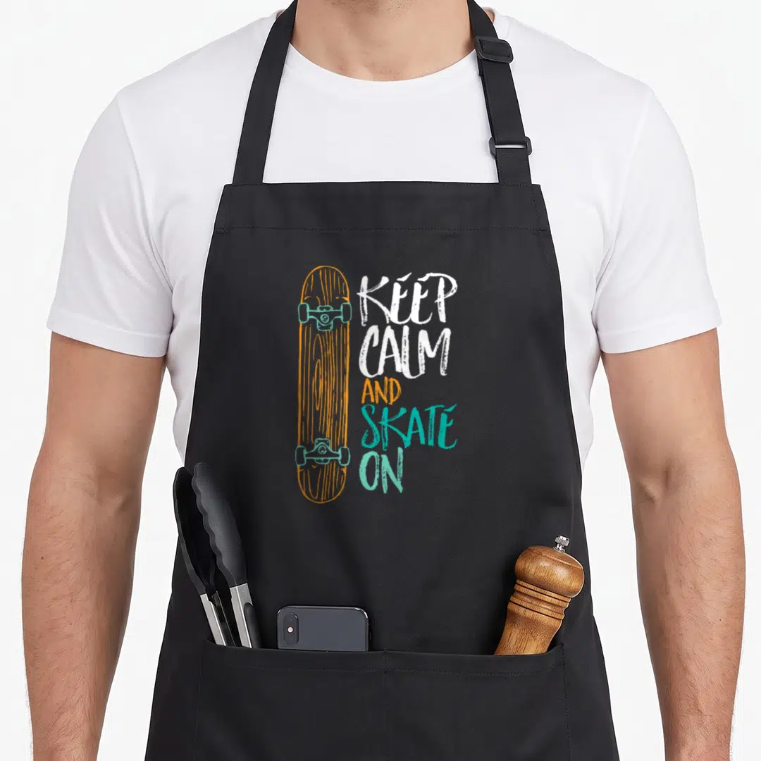 Skateboarding distressed apron - Vertical orange skateboard with teal trucks next to stacked white orange teal text — shown on a black cotton canvas apron against a white background