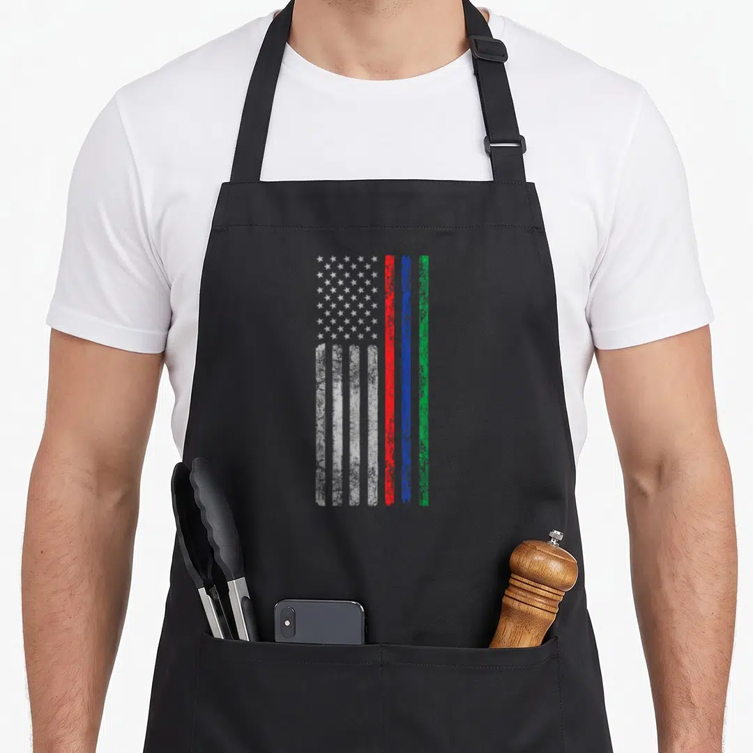 Military firefighter apron - Distressed flag with white stars and vertical red blue green stripes on black fabric — shown on a black cotton canvas apron against a white background